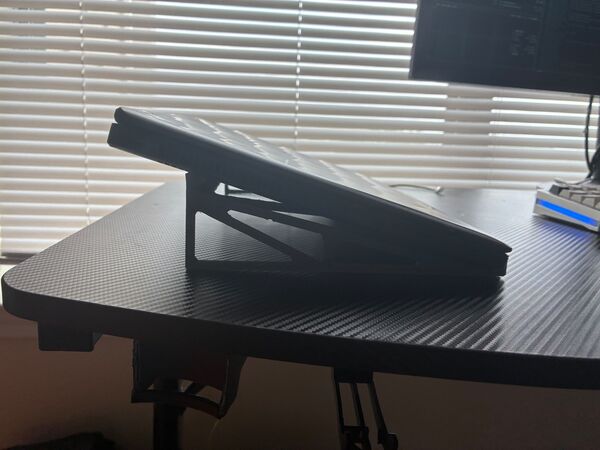 Side profile of a laptop on the stand, showing the shallow angle and open side truss.